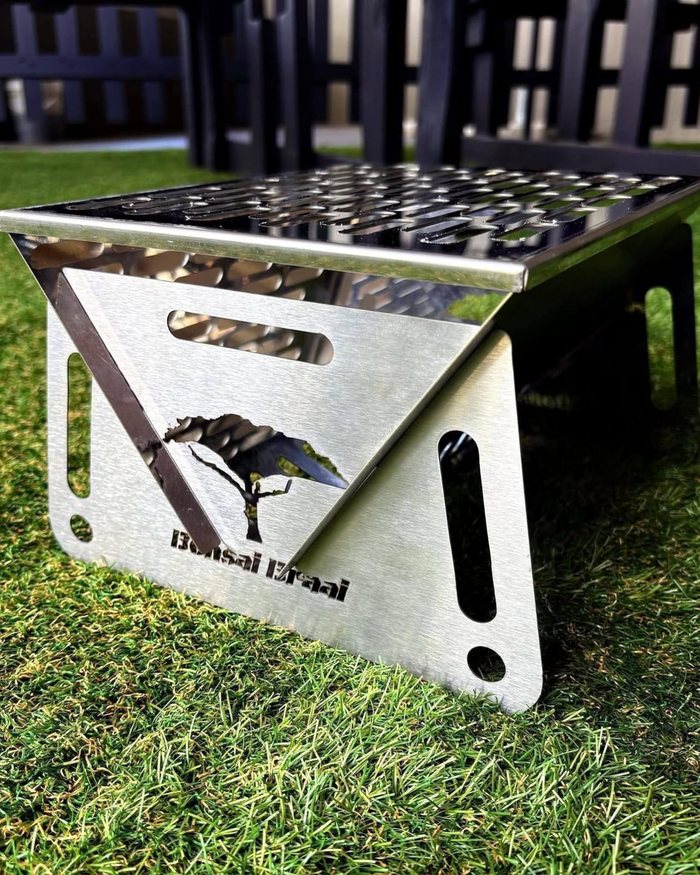 Die Bonsai Braai opgestel op gras: geborselde kante van 430 vlekvrye staal met 'n kameeldoring uitgesny.